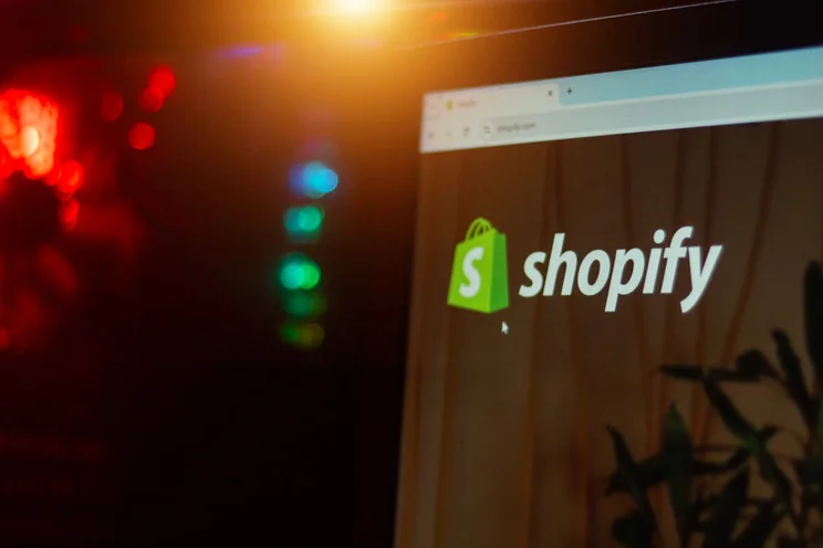 Close-up of a computer screen displaying the Shopify website logo with colorful lights in the background, hinting at a tech environment.