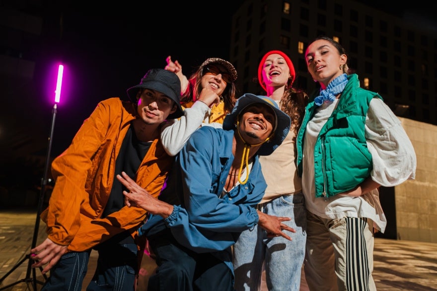 Social Media Trends for August Intro A group of five people in colorful streetwear poses playfully at night, with a vibrant pink light illuminating the background.