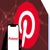 A hand holds a smartphone displaying the Pinterest logo, set against a blurred, red-backgrounded Pinterest symbol.