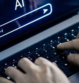 A person types on a laptop keyboard with a dark screen displaying