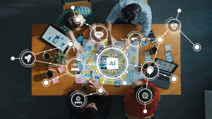 Team sitting and working around a table with icons floating above showing AI icons and other digital tools