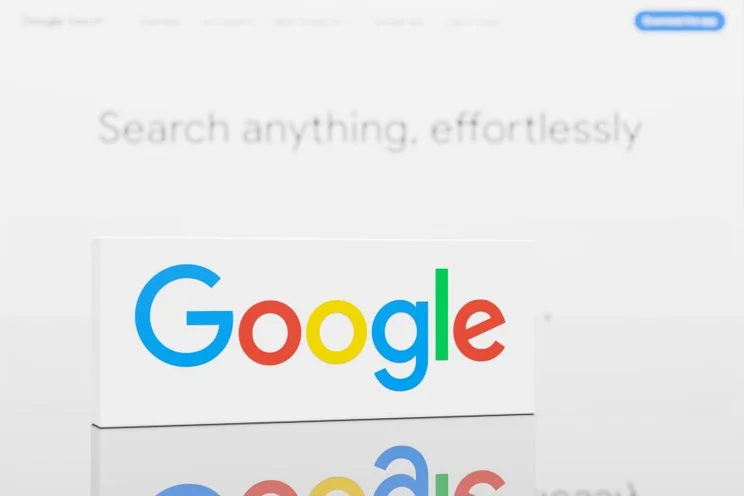 Close-up of Google logo on a white background with the text "Search anything, effortlessly" blurred in the rear.