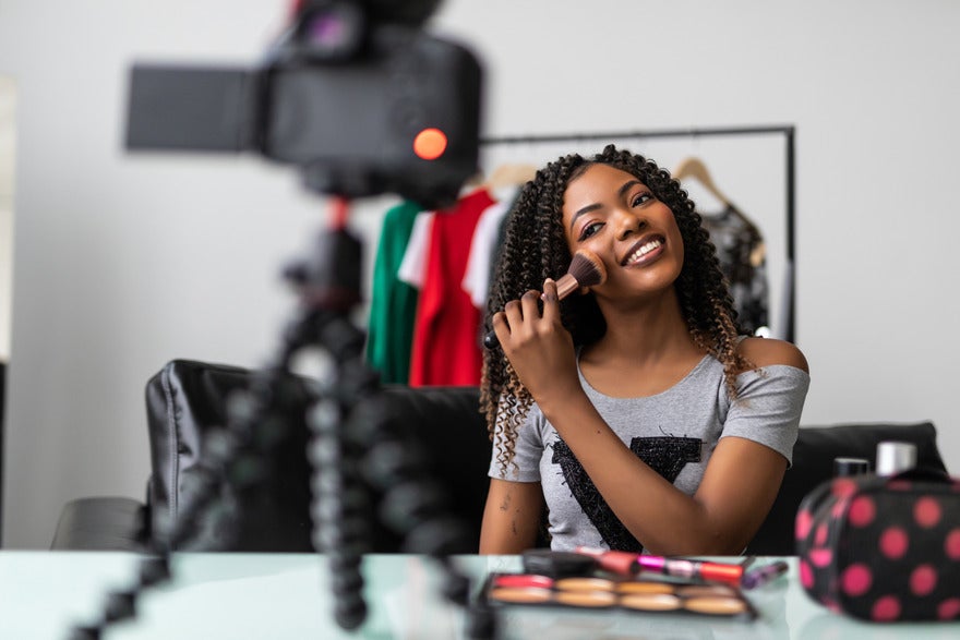 Person filming themself doing their makeup and smiling at the camera