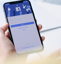 Person holding a phone showing the Facebook login