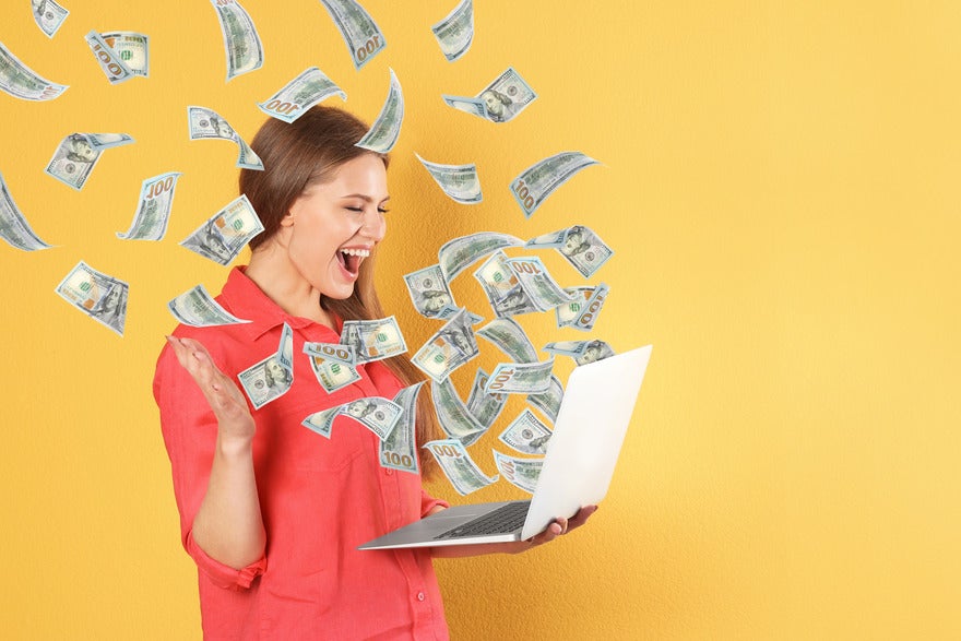 A person in a red shirt holds a laptop, surrounded by floating hundred-dollar bills against a bright yellow background.