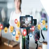 A smartphone on a gimbal captures a video in a kitchen, surrounded by animated social media reaction icons.