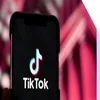 Mobile phone with TikTok logo, held against a red backdrop