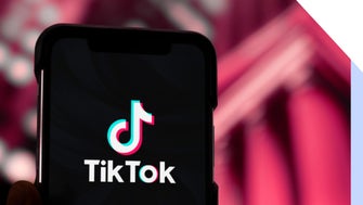 Mobile phone with TikTok logo, held against a red backdrop
