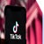 Mobile phone with TikTok logo, held against a red backdrop