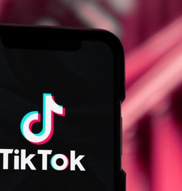 Mobile phone with TikTok logo, held against a red backdrop