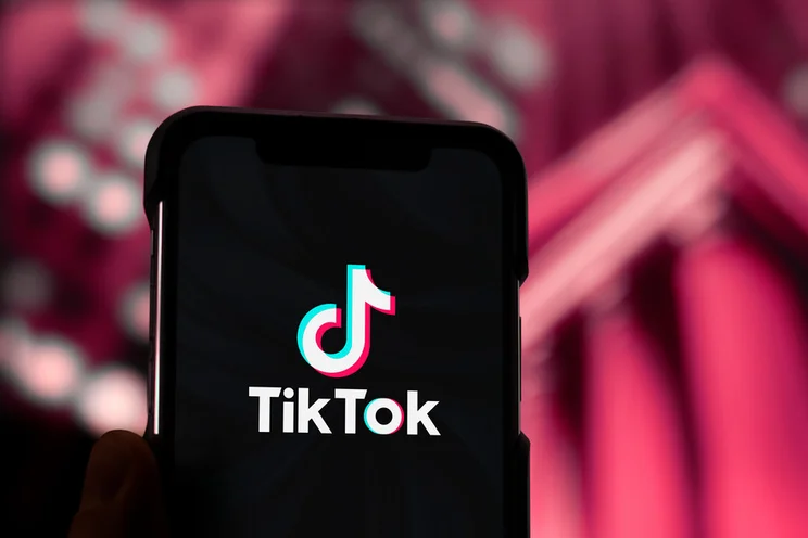 Mobile phone with TikTok logo, held against a red backdrop