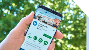 A person holding a smartphone displaying the "Bing Places for Business" app amidst a green blurred background.
