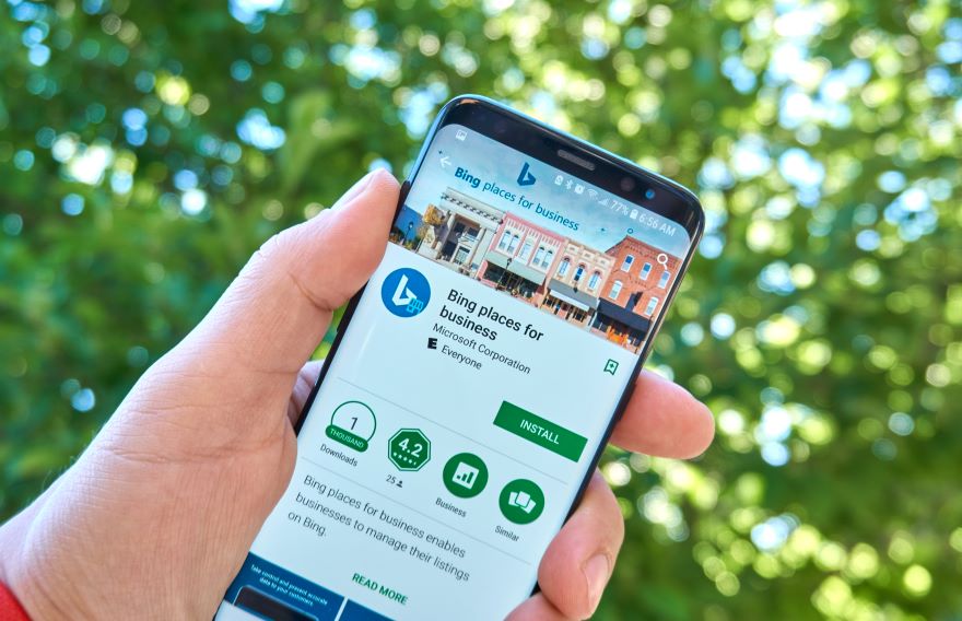 A person holding a smartphone displaying the "Bing Places for Business" app amidst a green blurred background.