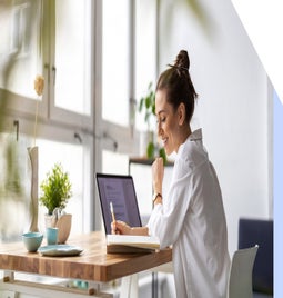 Woman working at her laptop on a desk by a large window