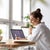 Woman working at her laptop on a desk by a large window