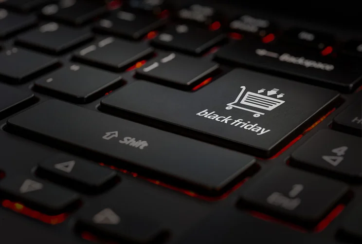 Close-up of a black keyboard highlighting a key labeled "black friday" with a shopping cart icon, set against a dimly lit background.