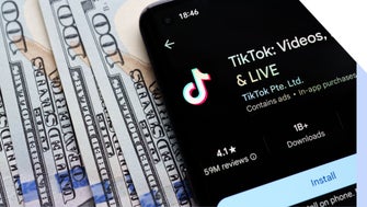 A smartphone displaying the TikTok app interface lies on a stack of hundred-dollar bills, highlighting digital media's connection to money.