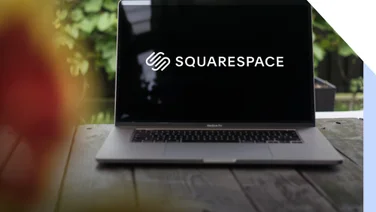 Laptop on a garden table with greenery in the background showing the Squarespace logo on the screen