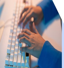 Hands typing at a white illuminated keyboard