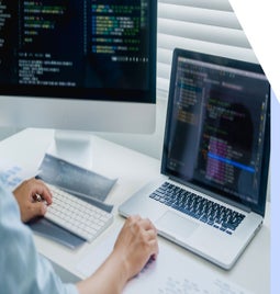 person coding on a laptop and a desktop screen