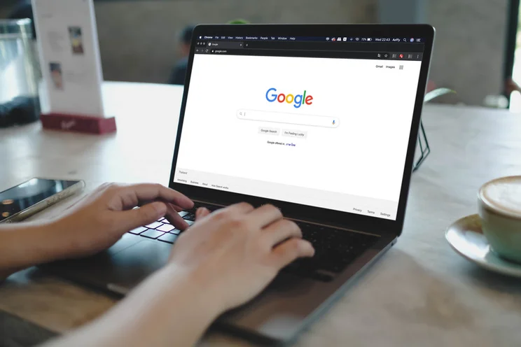 Hands typing at a laptop with the screen showing the Google homepage