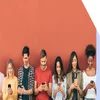 7 people leaning against a red wall looking down at their phones.