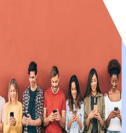7 people leaning against a red wall looking down at their phones.