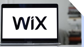A close-up of a MacBook Air displaying the Wix logo on its screen, with a blurred background of bookshelves.