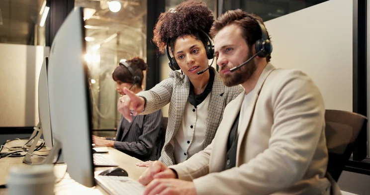 Two people looking at a computer screen with headsets on