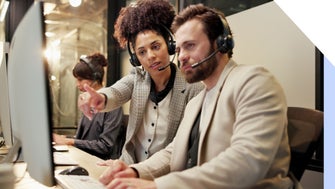 Two people looking at a computer screen with headsets on