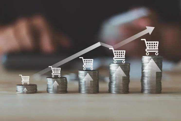 A stack of coins illustrating increasing growth, with shopping carts and upward arrows symbolizing rising sales or investments.