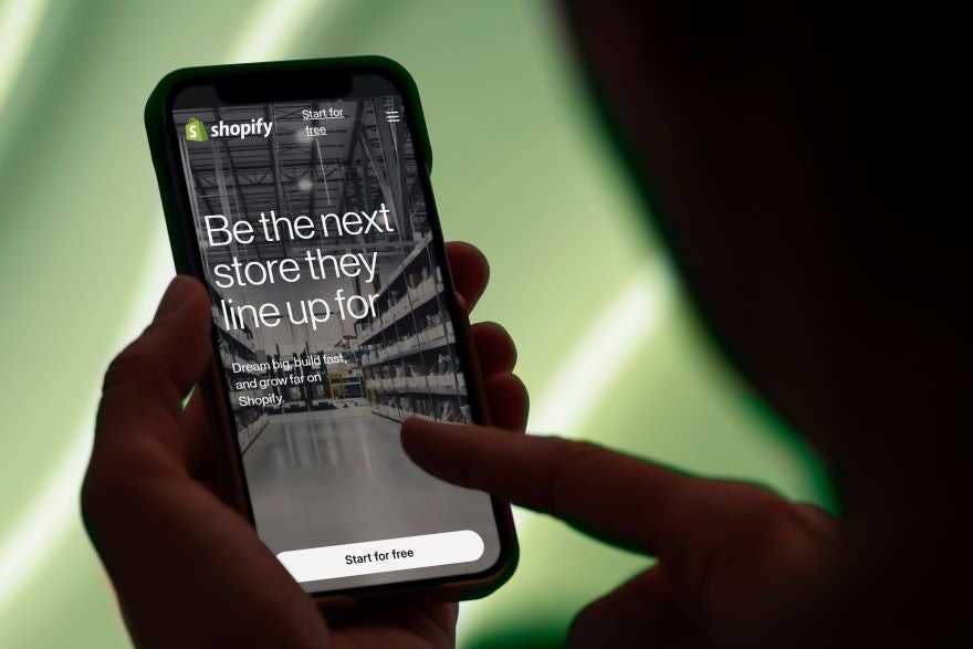 Person holding smartphone displaying Shopify website with the message: "Be the next store they line up for" and a "Start for free" button.