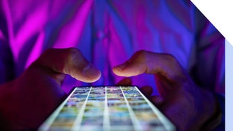A person holding a smartphone illuminated by colorful lights, scrolling through a grid of images on the screen.